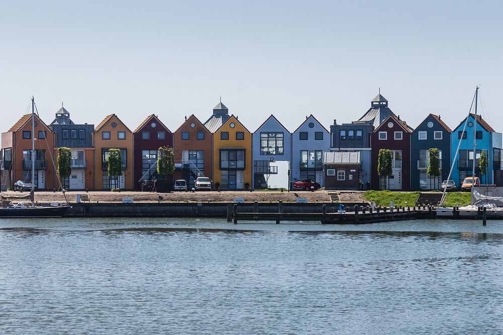 Rij kleurrijke woningen met puntgevels langs de kade van de haven van Stavoren, met zeilboten aan de steiger en water op de voorgrond